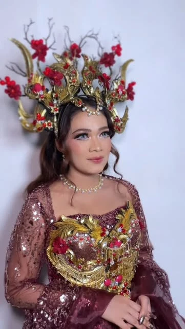 Rias carnival dengan kostum burgundy dan emas serta hiasan kepala bunga merah